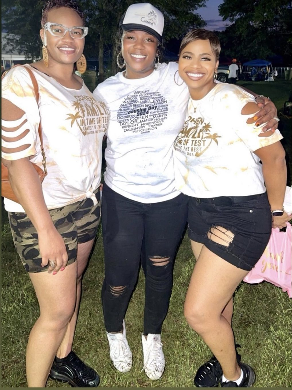 Three women in matching Cohen Family reunion shirts smiling at dusk